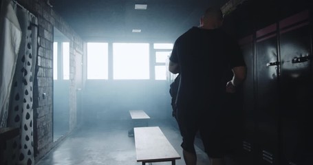 Camera follows young athletic Caucasian man entering dark gym locker room with backpack before workout slow motion.