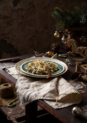 homemade russian traditional new year salad olivier with boiled vegetables, meat, pickles and mayonnaise on vintage green plate stand on wooden table with christmas tree branches, toys, grey napkin