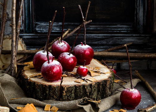 thanksgiving and halloween homemade red caramel glazed taffy apples with sticks on wooden board on sackcloth with tree branches opposite dark concrete wall