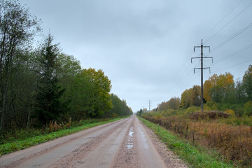 Fototapeta premium a dirt road runs along the forest. There is a high-voltage power line next to the road. The fall of the year