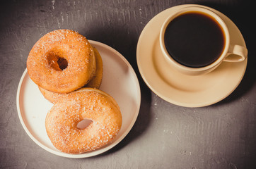 Doughnuts in a plate and a cup of black coffee. Top view. Dark textured background