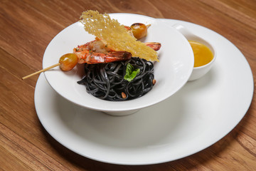 Black ink linguini pasta with roasted prawn skewer. Exquisite dish. Creative restaurant meal concept.	