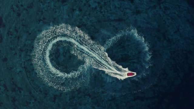Slowmotion aerial shot of a fast speedboat with a red roof top making an infinity shape in the clear turquoise magical sea. Love symbol. Top travel destination. 4K.