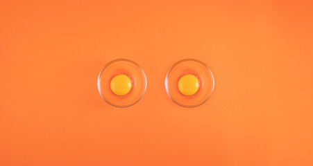 Two egg yolks in a glass cup isolated on orange background with space for text