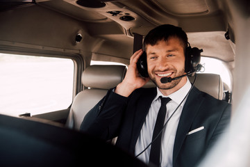 smiling bearded pilot in formal wear and headset sitting in plane