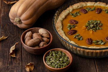 homemade pumpkin pie , pumpkin seeds and autumn leaves on a wooden background