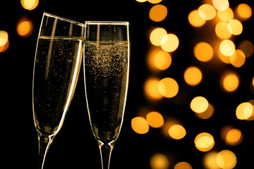 Two champagne glasses toasting on black background with bokeh lights, happy new year