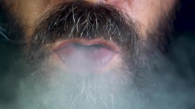 Slow motion video of the mouth of a bearded man exhaling smoke after smoking a CBD weed cigarette