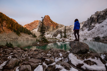 Adventurous Girl enjoying the View of a Glacier Lake in the Canadian Mountain Landscape during a colorful sunset in Fall. Taken in Watersprite Lake, Squamish, North of Vancouver, BC, Canada.