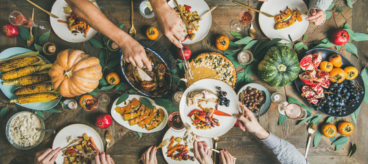 Thanksgiving or Friendsgiving holiday celebration party. Flat-lay of friends feasting at Thanksgiving Day table with turkey, pumpkin pie, roasted vegetables and fruit, top view, wide composition