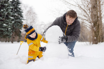 Little boy with his father building snowman in snowy park. Active outdoors leisure with children in...