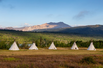 Beautiful View of the Tipi in a field with American Rocky Mountain Landscape in the background during a sunny summer morning. Taken in Montana near Glacier National Park, USA. - obrazy, fototapety, plakaty