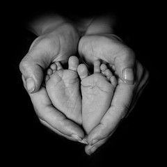 Madre envolviendo con sus manos los pies de su hijo recién nacido
