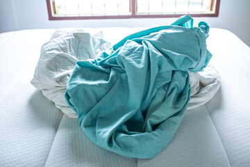 Turquoise and White crumpled bed sheet on white bed, Selective focus, Bedroom cleaning concept