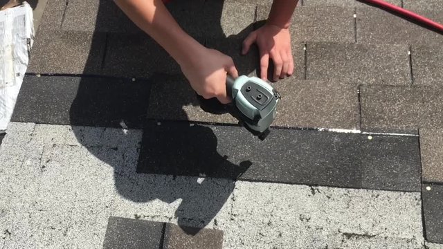 Nail fun in slow motion from above as roofer affixes shingles over existing roof. 