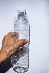 Senior woman's hand squashing used plastic bottle, Water drops on transparent soft drink ,  White background, Light & Shadow,  Close up shot, Environment, Global warming, Recycle concept