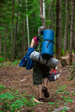 Diverse People Enjoy Spiritual Gathering A Middle Aged Man Is Seen Walking Through Dense Woodland Carrying Backpacks, A Tent And Camping Equipment, Seeking A Scared Ground For Mindful Retreat.