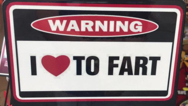 Funny generic warning I love to fart sign close up swaying in breeze.