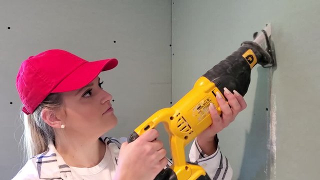 Woman in construction with reciprocating saw cutting sheetrock wall