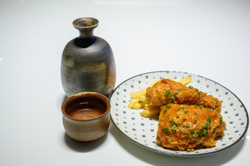 Fried chicken on a polka dot dish, complete with bottles and sake cups made from ancient terracotta on a white background. It's a Japanese style meal.