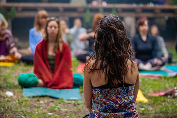 Diverse people enjoy spiritual gathering A close up & rear view of a spiritual leader teaching mindful meditation at a rural retreat, blurry people are seen sitting in background with copy-space.