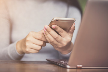 female holding smartphone getting message with confirmation making transaction on laptop computer