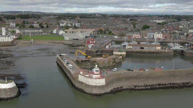 An aerial view of Arbroath harbour and town on a cloudy day. Left to right circling view of the harbour with the town in the background.