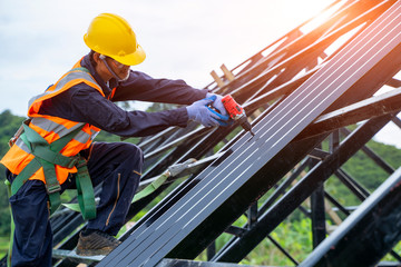 Roofer worker in protective uniform wear and gloves, using air or pneumatic nail gun and installing asphalt shingle on top of the new roof,Concept of residential building under construction.