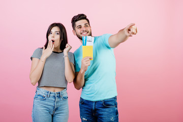 handsome young couple man and woman with passport and plane tickets isolated over pink