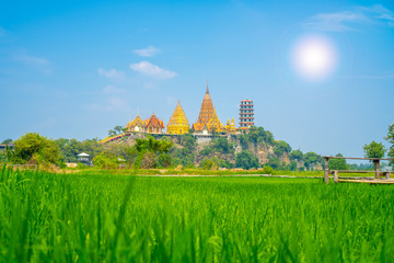 Obraz premium Scenery view at Wat tham sua or tiger cave temple with green jasmince rice field,blue sky ,sun shine and long walkway bamboo bridge. Tourist attraction in Kanjanaburi.