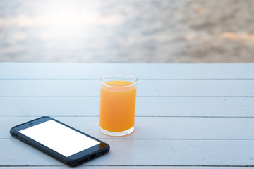 Orange juice in glass and mobile phone on white wooden table
