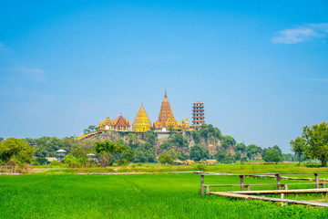 Scenery view  at Wat tham sua or tiger cave temple with green jasmince rice field,blue sky ,sun shine and long walkway bamboo bridge. Tourist attraction in Kanjanaburi.