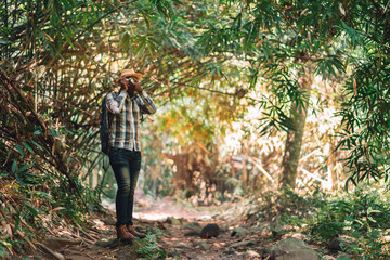 African man traveller using camera with backpack standing in the green natural forest.