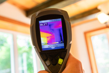 Indoor damp & air quality (IAQ) testing. A closeup view of an infrared thermal vision device, pointing towards the ceiling and large windows of a residential property, checking for cold bridging. - obrazy, fototapety, plakaty