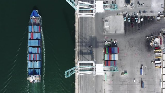 4K. Aerial topdown view over the docks of Port Miami and the container ship following along the wharf. The view of port infrastructure from the air. port cranes, parking lots, multi-colored containers