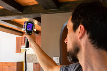 Indoor damp & air quality (IAQ) testing. An indoor environment quality (IEQ) assessor is seen at work, using a digital thermography device during an in-depth inspection of a domestic building.