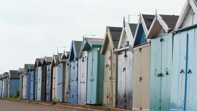 4K Man Running along  British Seaside Beach Huts at a Coastline in a UK Resort in Britain. Summer Holiday Pastel painted wooden Chalets for recreation, storage and tourism.