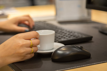 Woman hand holdding coffee cup with working table