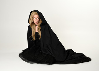 full length portrait of blonde girl wearing long black flowing cloak, sitting on the floor  with  a...