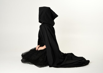 full length portrait of blonde girl wearing long black flowing cloak, sitting on the floor  with  a...