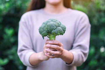 a woman holding and giving a green broccoli in hands