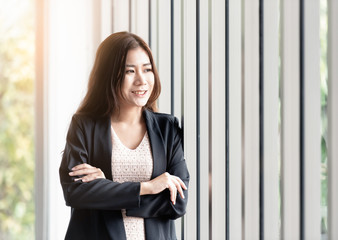 One working beautiful women standing near the window in the office. She stood and crossed her arms and looked outside and was thinking of a big project.