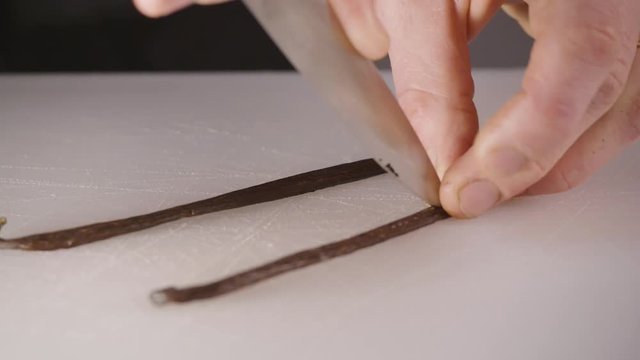 A chef delicately slices open a vanilla bean and extracts the vanilla using a very sharp knife.
