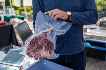 Fresh food at outdoor farmer's market. A close up view of a local butcher holding a large t-bone...