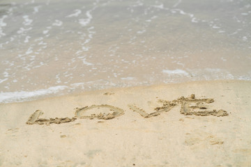 Love written on sand, in the background soft waves with foam of ocean on the sandy beach.