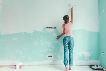 Preteen child painting the wall in her room in blue and white colors. Young girl making interior...