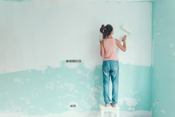 Preteen child painting the wall in her room in blue and white colors. Young girl making interior...
