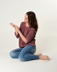 full length portrait of brunette woman wearing jeans and pink jumper. seated pose with a white...