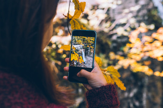 woman taking picture of autumn waterfall on the phone