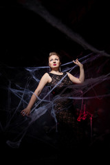 Fototapeta na wymiar Woman in evening classic dress posing on black Halloween background with spider web